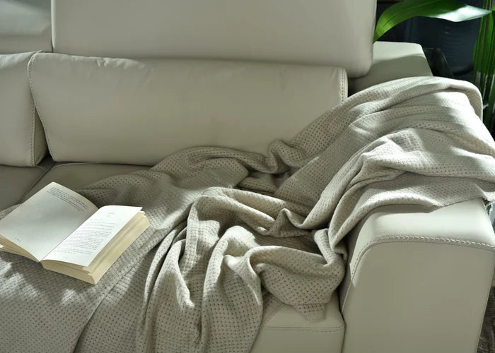Light brown knitted throw blanket with textured weave, draped over sofa arm.