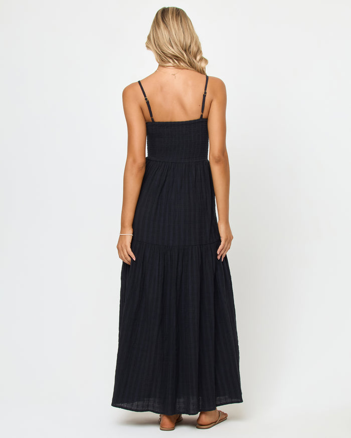Back view of a model wearing the LSPACE Mabel Maxi Dress in black, showing the smocked back bodice and tiered maxi skirt.