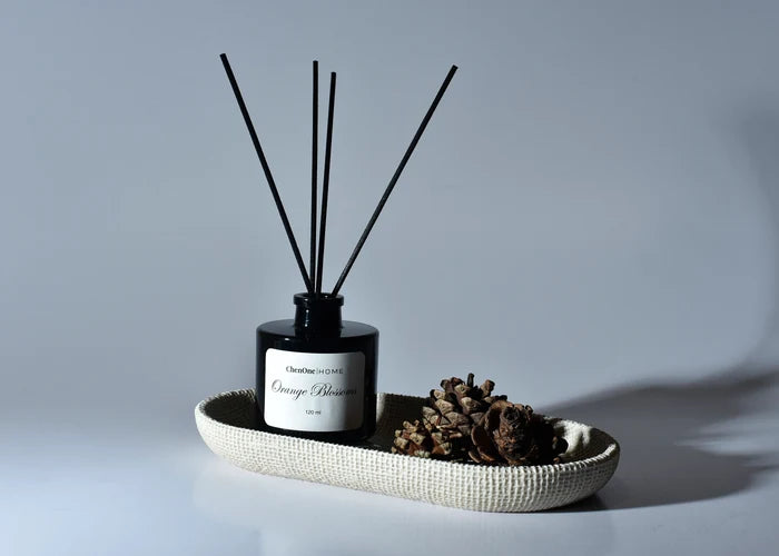 Reed diffuser bottle with dark reeds on textured tray with pine cones