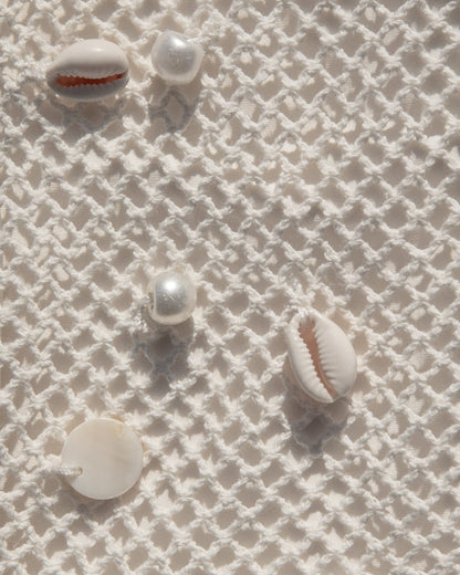 Close-up of cream open-knit crochet fabric with natural shell embellishments.