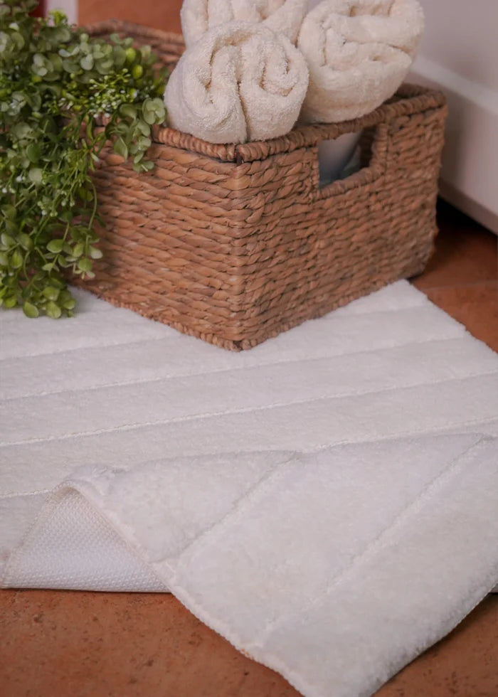 White polyester bath mat with textured surface, corner hem visible