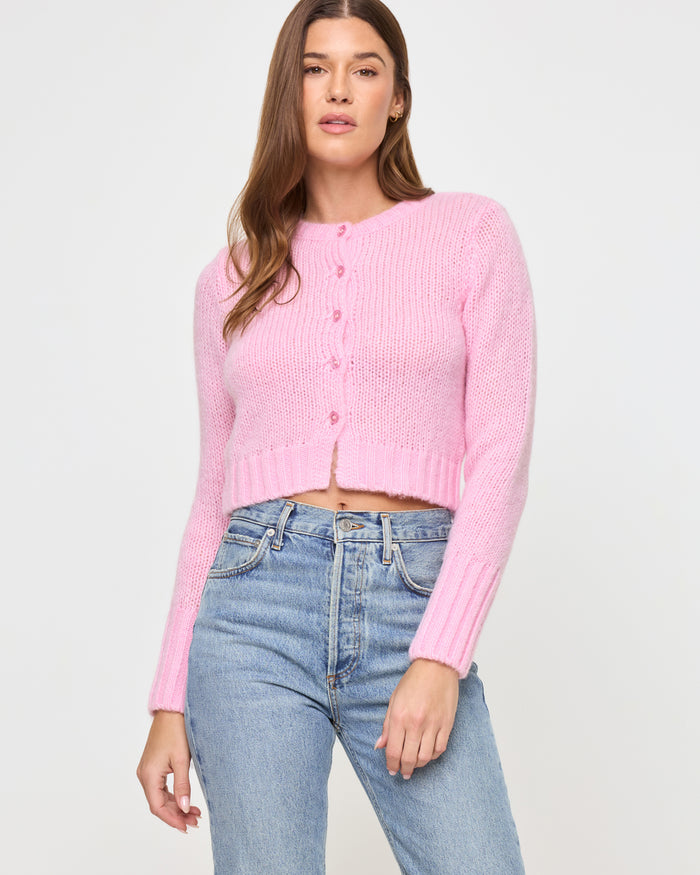 Front view of a model wearing the LSPACE Brynn Cardigan in rosewater, a cropped pink knit cardigan with button-front closure and long sleeves.