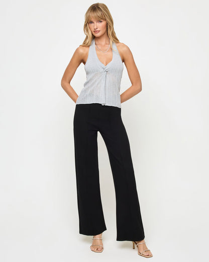 Front view of a model wearing the LSPACE Callie Halter in metallic silver, featuring the deep V-neckline with a twist-front detail and halter neck in semi-sheer metallic knit fabric, styled with black wide-leg flare trousers and strappy heeled sandals.