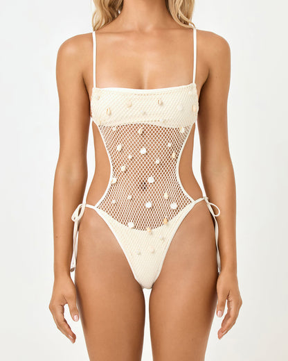 Close-up front view of a model wearing the LSPACE cream Catching Up One Piece with the crochet bodice, sheer mesh midsection with pearl and shell embellishments, and side tie details.