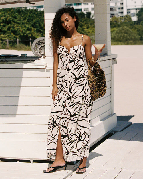 Front view of a model wearing the LSPACE Chara Maxi Dress in heavy petal, a black and white abstract leaf print maxi dress with spaghetti straps and a front slit, photographed at an outdoor beachside setting.