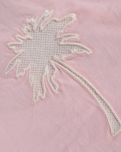 A close-up of a light pink fabric featuring a white embroidered palm tree motif.