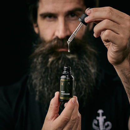 Bearded man holding a dropper of Night Liquid Elixir beard oil above the open bottle. The Beard Struggle