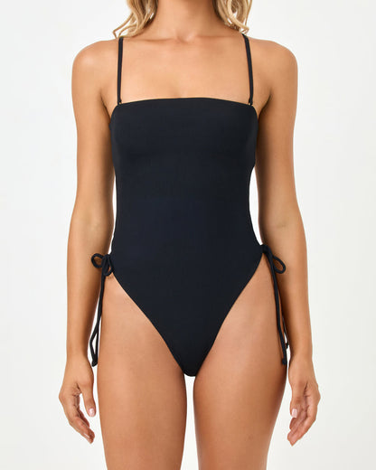 Close-up front view of a model wearing the LSPACE black Elise One Piece Swimsuit showing the straight bandeau neckline with gold ring hardware and adjustable side ties.