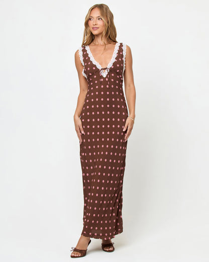 Front view of a model wearing the LSPACE Eyes On You Maxi in Alotta Polka Dot on a white background, a brown maxi dress with large pink polka dots, white lace trim V-neckline, tie-front waist, and side slit, styled with brown heeled sandals.