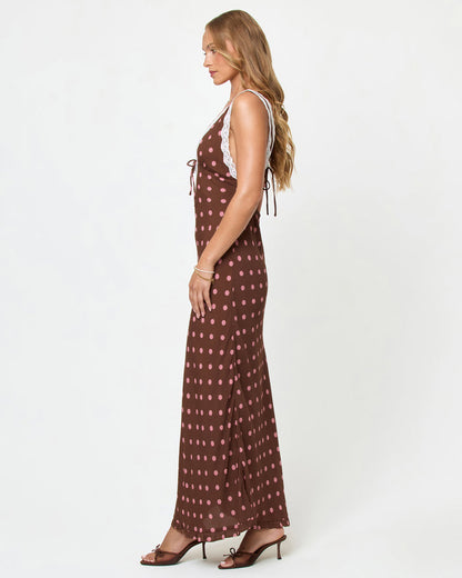Side view of a model wearing the LSPACE Eyes On You Maxi in Alotta Polka Dot on a white background, showing the full-length silhouette of the brown polka dot maxi dress.