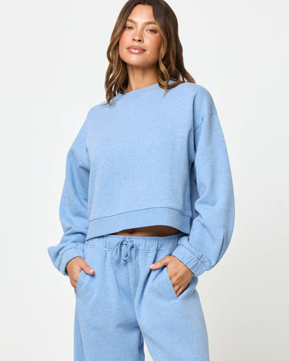 Front full-length studio view of the Fleur Sweatshirt and Fleur Pant in chambray blue, a chambray blue cropped crewneck sweatshirt with balloon sleeves paired with chambray blue wide-leg drawstring jogger pants, styled together as a set.
