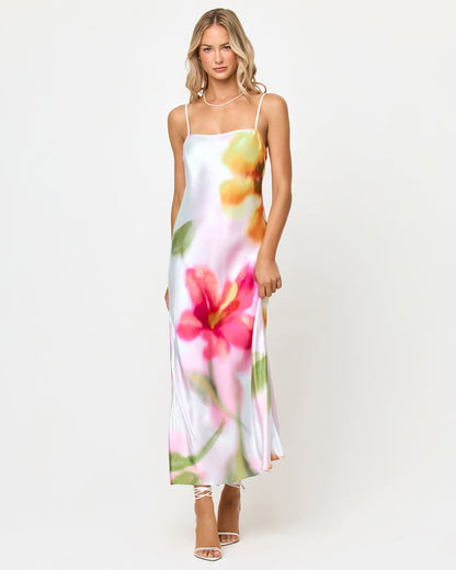 Front view of a model wearing the LSPACE Gabby Maxi in soft focus, showing the full-length satin silhouette with thin spaghetti straps, cowl neckline, and dreamy soft-focus floral print in pink, coral, yellow, and green.