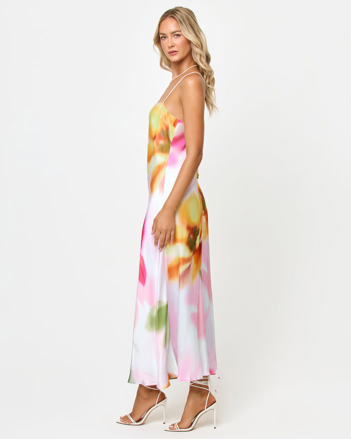 Side view of a model wearing the LSPACE Gabby Maxi in soft focus, showing the bias-cut satin silhouette and strappy back detail with the blurred floral print.