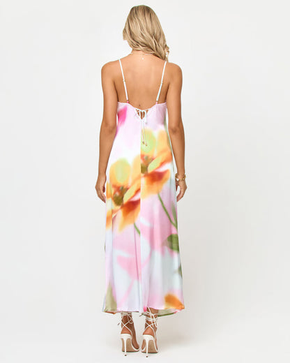 Back view of a model wearing the LSPACE Gabby Maxi in soft focus, highlighting the strappy back tie detail and the soft-focus floral print in yellows, oranges, and pinks on the satin maxi dress.