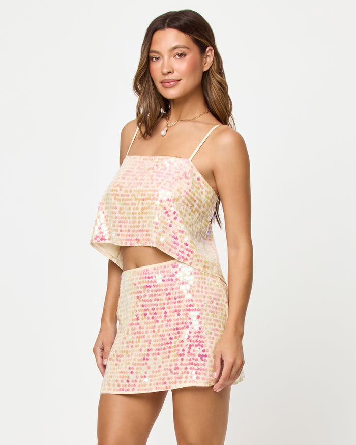 Three-quarter front view of a model wearing the LSPACE Glow Getter Top and Skirt in prosecco, an iridescent sequin mini skirt in champagne and pink tones.