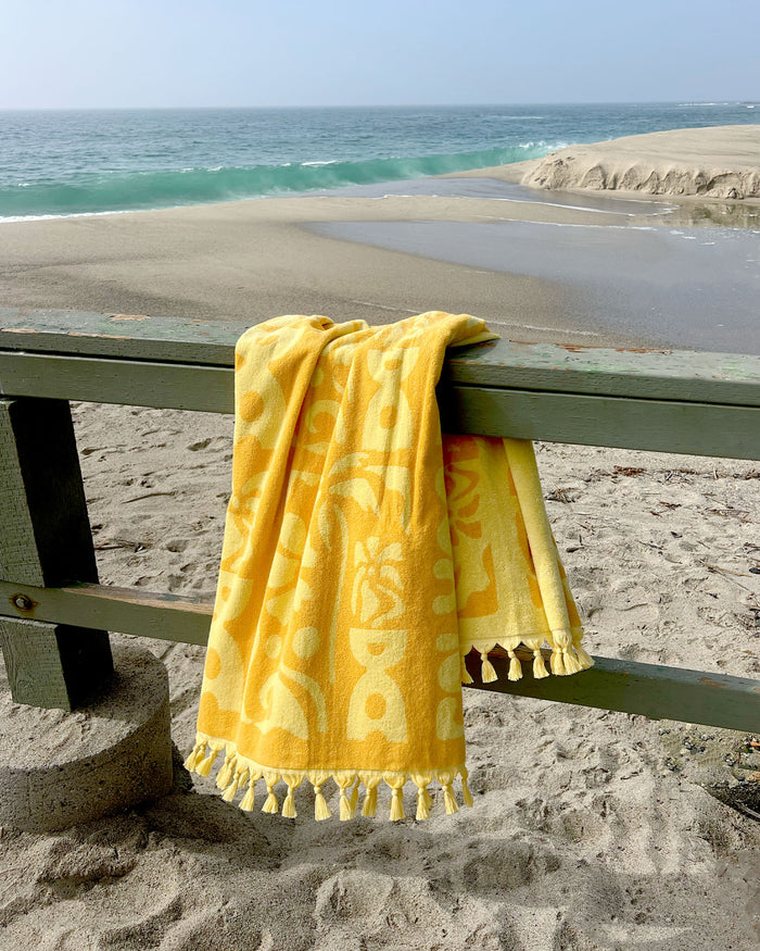 LSPACE Holiday In The Sun towel, off-model flat lay draped on a railing at the beach.