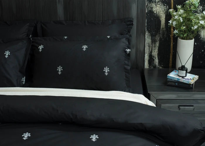 6-piece black comforter set with white floral cross motif, stacked pillows detail
