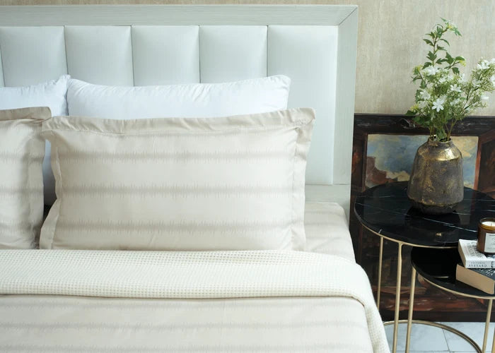 Single beige cotton bed sheet set with pillow shams and folded top sheet on bed
