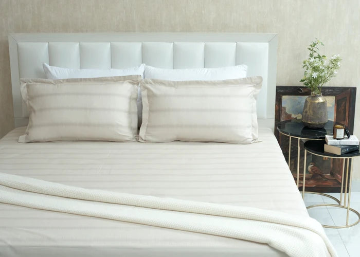 Single beige cotton bed sheet set with two pillow shams, neatly laid on the bed
