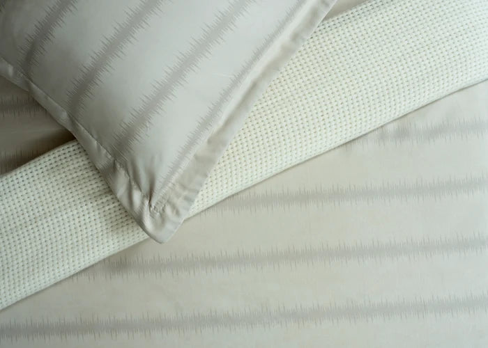 Beige cotton bed sheet fabric with subtle textured weave, close-up fold
