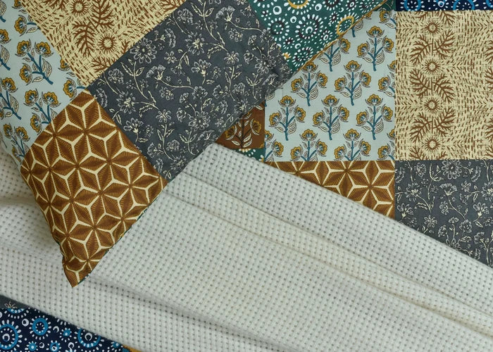 Cotton bed sheet detail with cream small-dot texture and navy floral corner accents