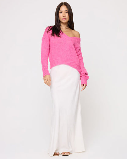 Front view of a model wearing the LSPACE Icon Pullover - Bubblegum Pink in bubblegum pink, an oversized knit pullover worn with an off-shoulder neckline, styled with a white maxi skirt.