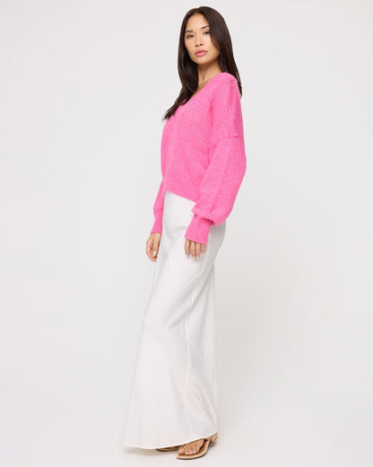 Side view of a model wearing the LSPACE Icon Pullover - Bubblegum Pink in bubblegum pink, showing the oversized silhouette and long ribbed cuffs of the knit pullover, styled with a white maxi skirt.