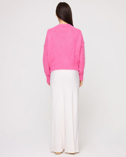 Back view of a model wearing the LSPACE Icon Pullover - Bubblegum Pink in bubblegum pink, showing the back of the oversized knit pullover, styled with a white maxi skirt.