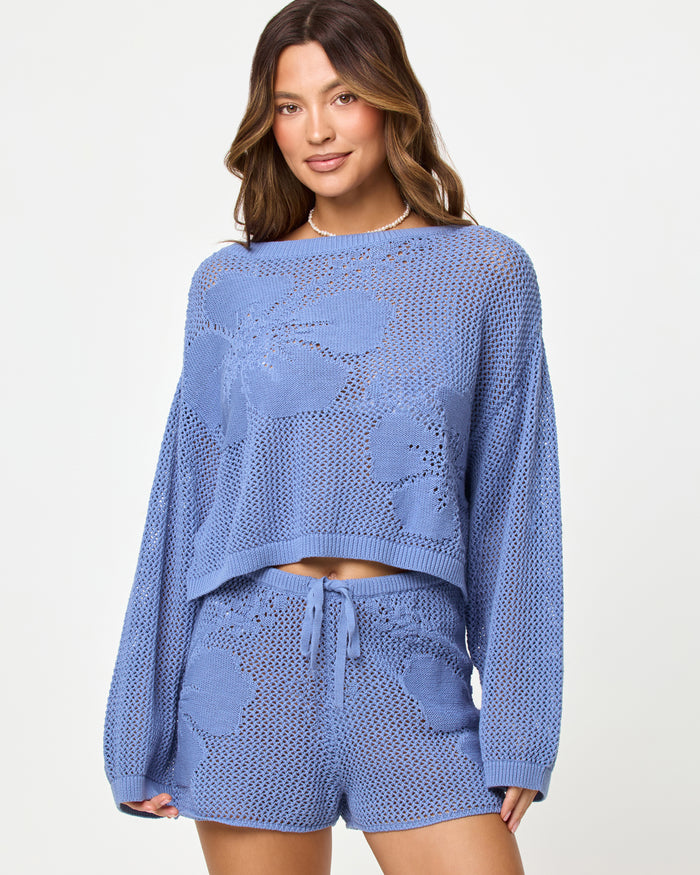 Close-up of a model wearing the LSPACE Island Time Short in Chambray, styled with the matching Island Time Sweater, highlighting the open-knit crochet floral design and drawstring waist.