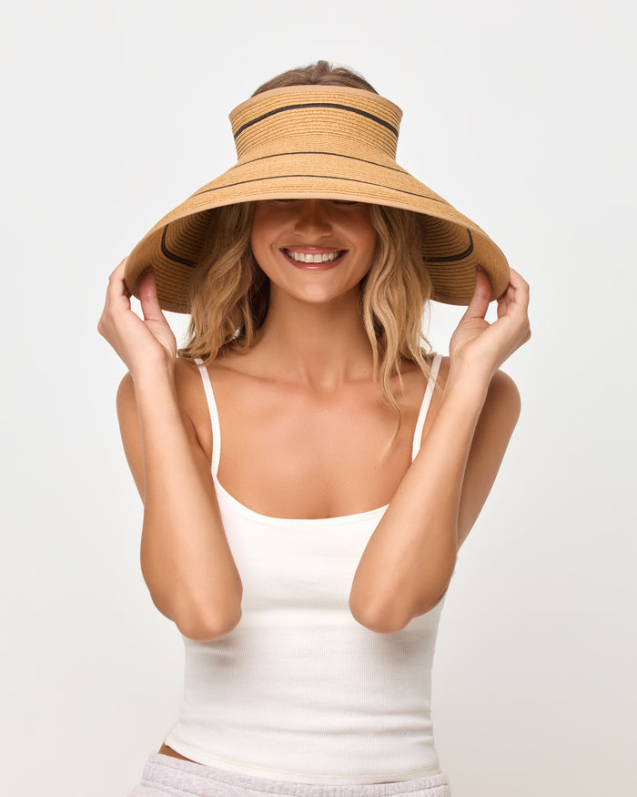 Front view of a smiling model pulling the brim of the natural and black Jess Roll Up Hat down over her eyes, wearing a white tank top.