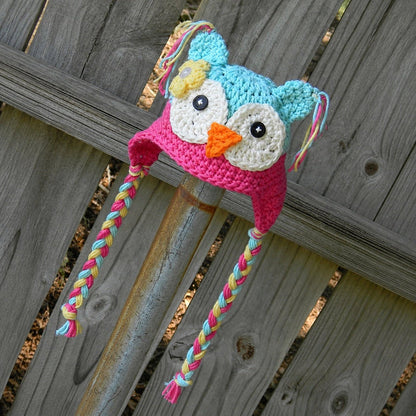 Light blue and rose owl beanie with braided ties on wooden background