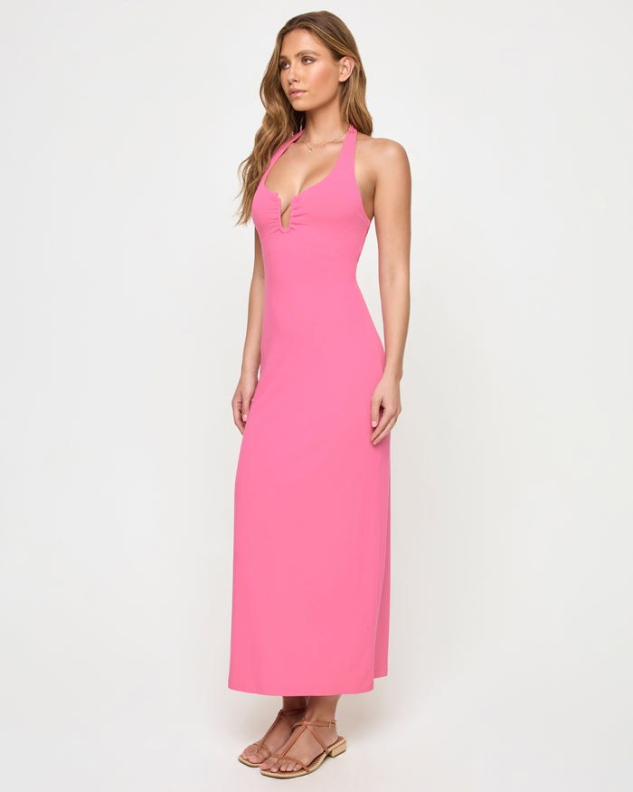 Side view of a model wearing the LSPACE La Femme Dress in begonia, showing the fitted silhouette and deep V-neckline of the halter dress.
