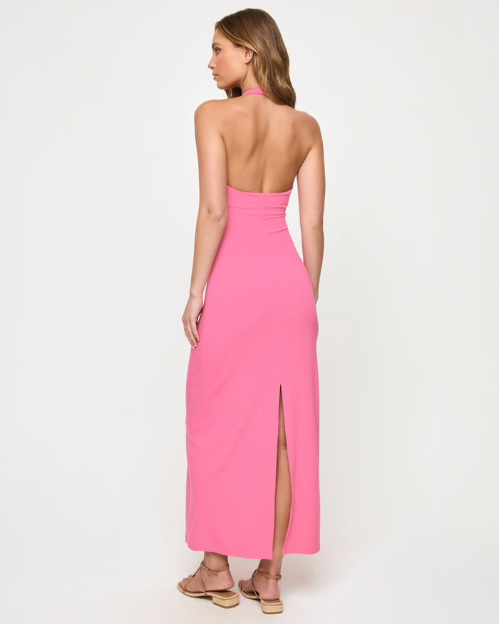 Back view of a model wearing the LSPACE La Femme Dress in begonia, showing the low open back, halter neck tie, and back slit at the hem.