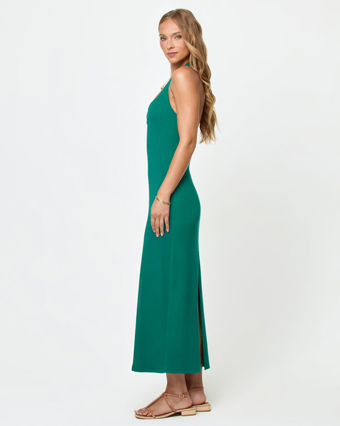 Side view of a model wearing the LSPACE La Femme Dress in Isle on a white background, showing the silhouette of the fitted emerald green ribbed knit halter maxi dress with a side slit at the hem.