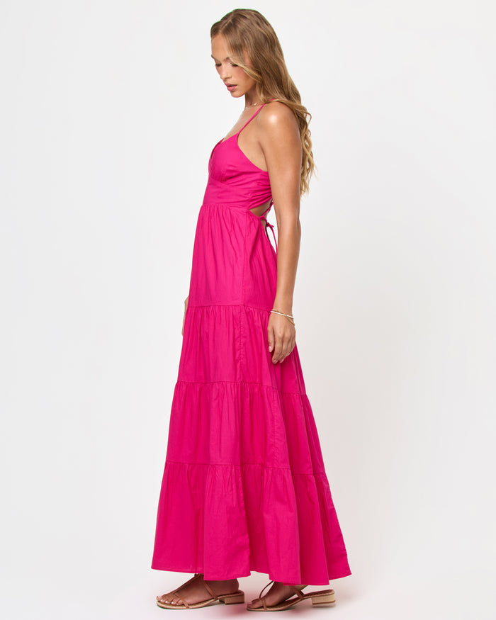 Side view of a model wearing the LSPACE Laina Dress in Bougainvillea on a white background, showing the side cutout and ruched waist detail of the hot pink tiered maxi dress.