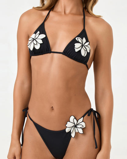Close-up on model detail of the LSPACE black Aspen Bikini Top and Levy Bikini Bottom highlighting the white plumeria flower appliqué and side tie.