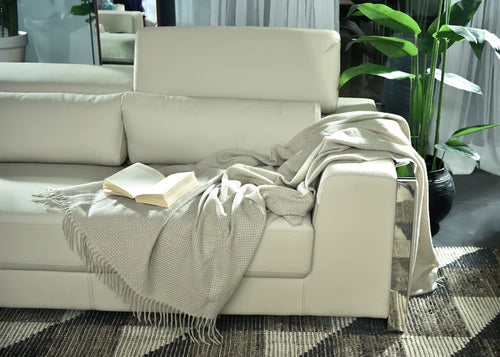 Light brown knitted throw blanket with fringed edge, folded on sofa.