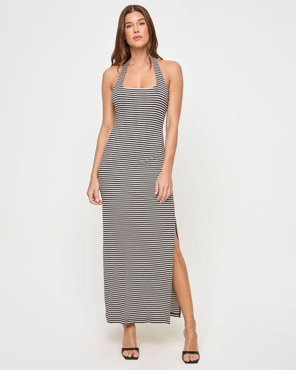 Front view of a model wearing the LSPACE London Dress in see both sides stripe, a fitted maxi dress with a square neckline, halter back strap, horizontal black and cream stripes, and a side slit at the hem.