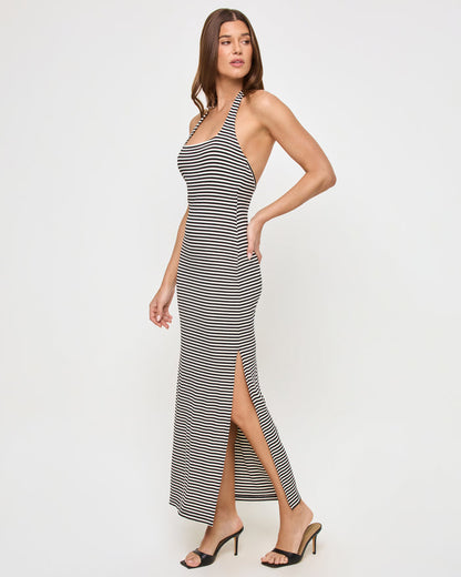 Side view of a model wearing the LSPACE London Dress in see both sides stripe, showing the fitted silhouette, halter neck strap, and the side slit on the black and cream striped maxi dress.