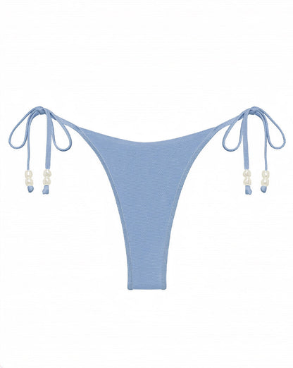 Off-model flat lay of the LSPACE chambray Lucia Bikini Bottom showing the double side ties with pearl bead accents, styled with a matching Sunrise Shell bikini top