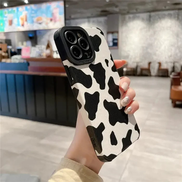 a woman holding up a cell case with a cow pattern