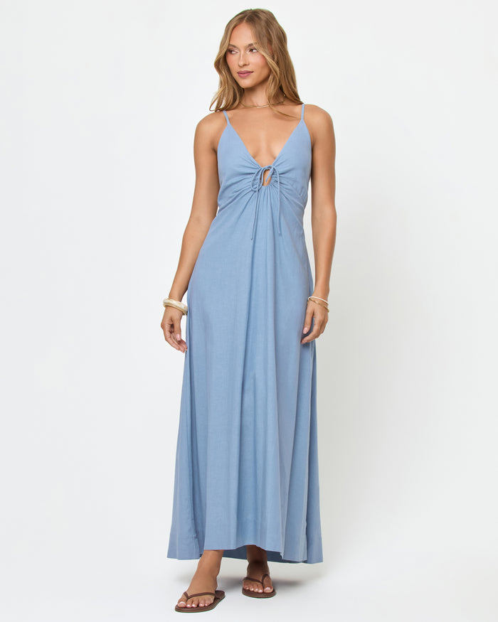 Front view of a model wearing the LSPACE Mabel Maxi Dress in chambray, a soft blue maxi dress with thin spaghetti straps, a deep V-neckline with ring drawstring detail, and a flowing A-line skirt.