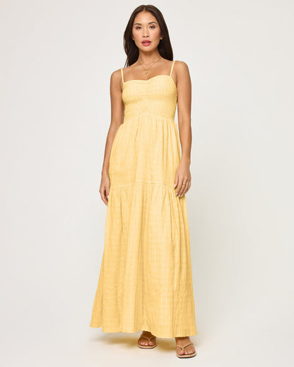 Front view of a model wearing the LSPACE Mallorca Dress in daisy, a soft yellow maxi dress with a ruched smocked bodice, thin spaghetti straps, and a tiered flowing skirt.