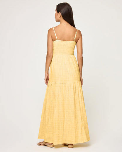 Back view of a model wearing the LSPACE Mallorca Dress in daisy, showing the smocked back bodice with adjustable spaghetti straps and the flowing tiered maxi skirt.