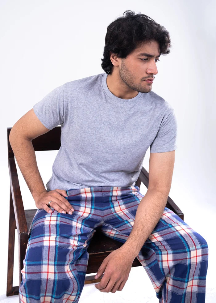 Men's grey melange T-shirt with blue-red plaid night pants, seated pose