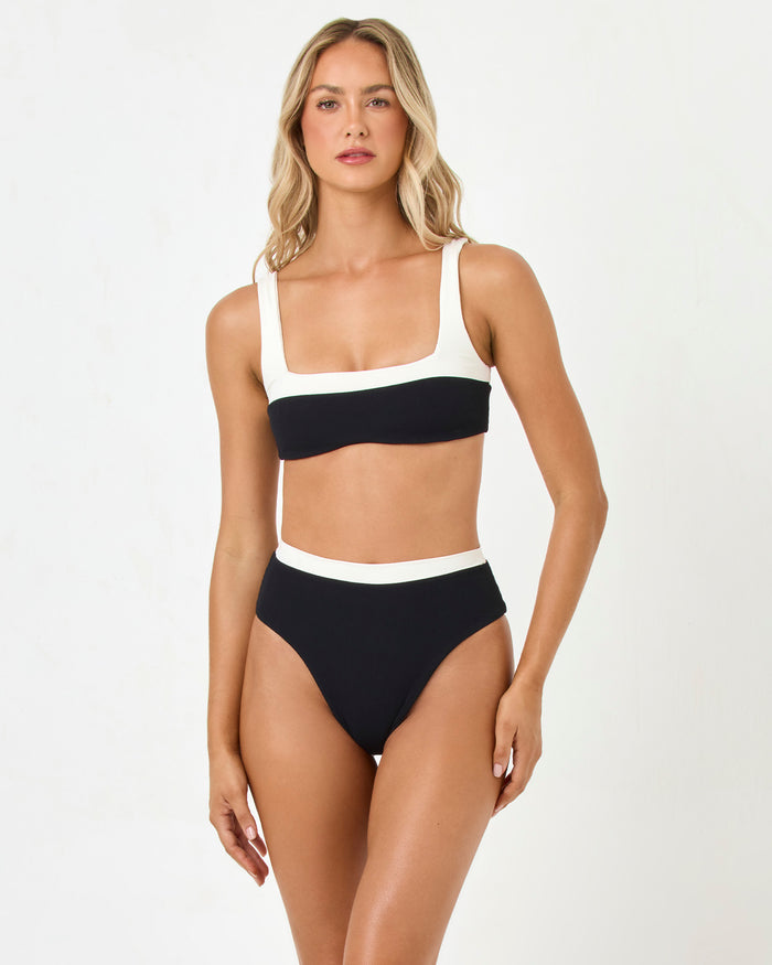 Front view of a model wearing the LSPACE black-cream Misha Bikini Bottom with cream waistband trim and matching Zuri Bikini Top.