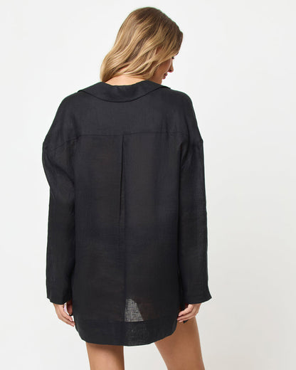 Back view of a model wearing the LSPACE Oasis Tunic in black as a cover-up, showing a collared neckline, long sleeves, a center back panel, and a relaxed oversized silhouette.