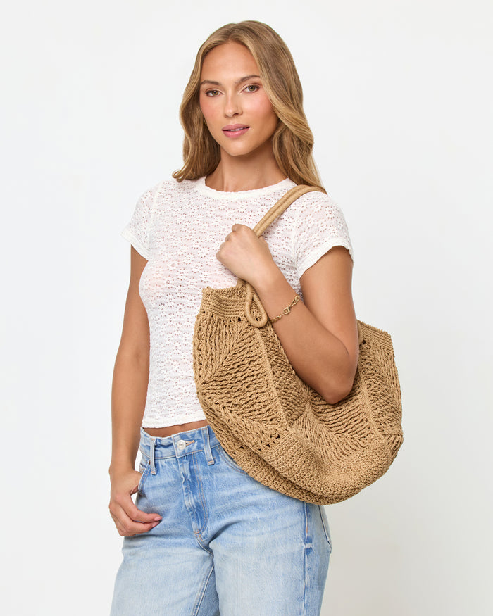 Front view of a model carrying the natural Paloma Beach Tote on her shoulder, wearing a white lace crop tee and light blue jeans.