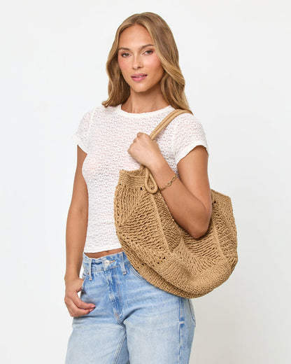 Front view of a model carrying the natural Paloma Beach Tote on her shoulder, wearing a white lace crop tee and light blue jeans.