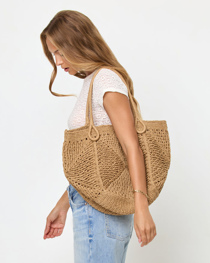 Side view of a model carrying the natural Paloma Beach Tote on her shoulder, wearing a white lace crop tee and light blue jeans.
